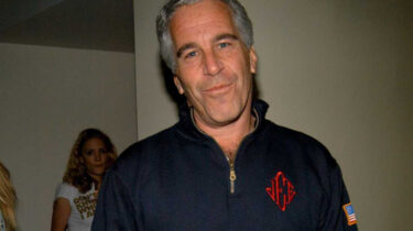 Man in dark zip-up sweater believed to be Jeffrey Epstein smirking at camera