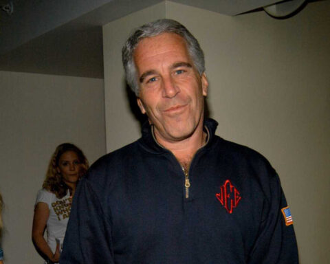 Man in dark zip-up sweater believed to be Jeffrey Epstein smirking at camera