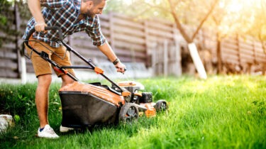 Man mowing lawn with shirt on in backyard