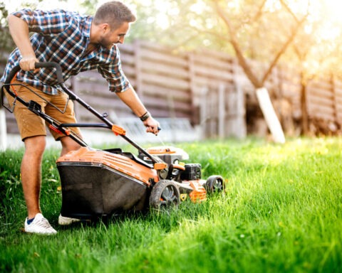 Man mowing lawn with shirt on in backyard