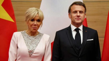 French President Emmanuel Macron and First Lady Brigitte Macron standing in front of flags