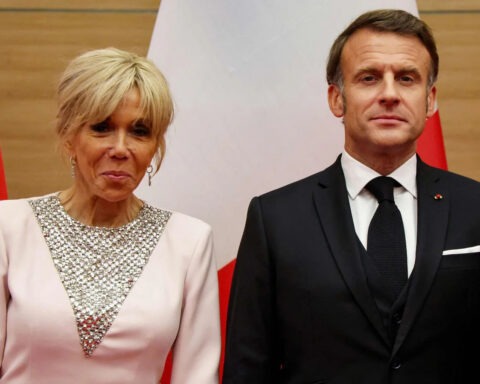 French President Emmanuel Macron and First Lady Brigitte Macron standing in front of flags