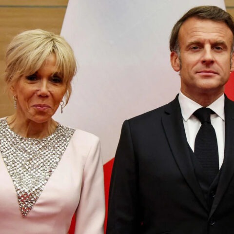 French President Emmanuel Macron and First Lady Brigitte Macron standing in front of flags