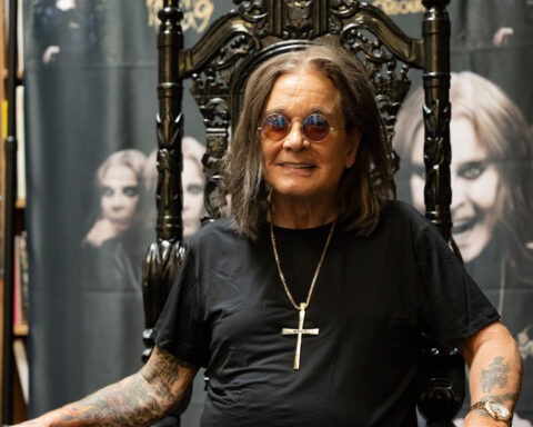 Ozzy Osbourne smiling in sunglasses and black shirt on gothic throne