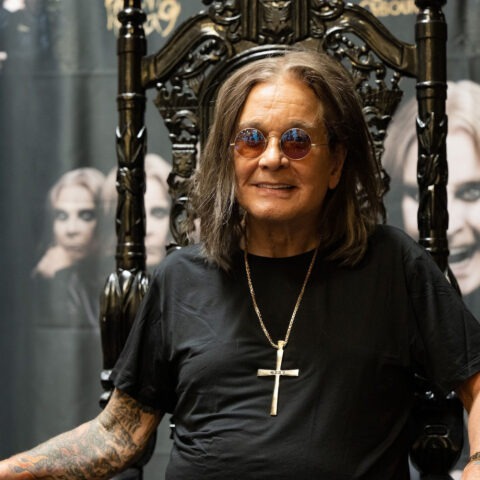 Ozzy Osbourne smiling in sunglasses and black shirt on gothic throne