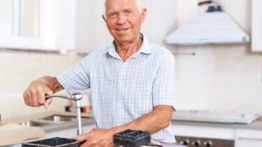 Retired man smiling while adjusting a working kitchen faucet with tools