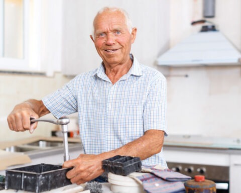 Retired man smiling while adjusting a working kitchen faucet with tools