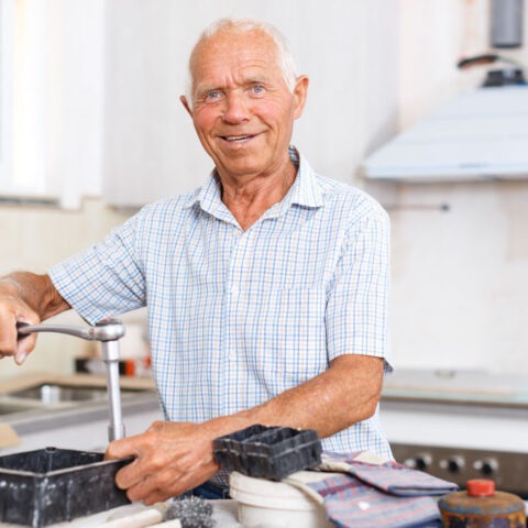 Retired man smiling while adjusting a working kitchen faucet with tools