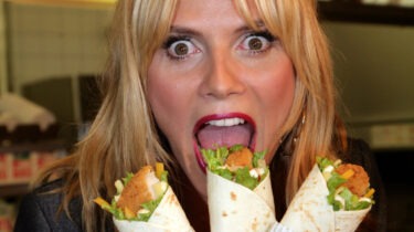Woman with shocked expression holding three McDonald’s Snack Wraps near her open mouth