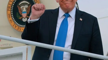 Donald Trump smiles and raises his fist while stepping off Air Force One