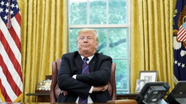 Donald Trump sits with arms crossed at Oval Office desk