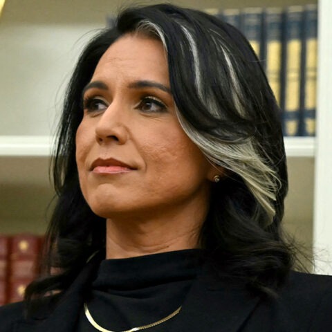 Tulsi Gabbard standing in front of U.S. Navy flag and bookshelf