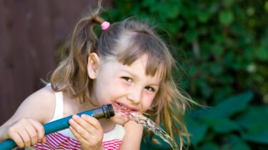 Child happily drinking water from a garden hose
