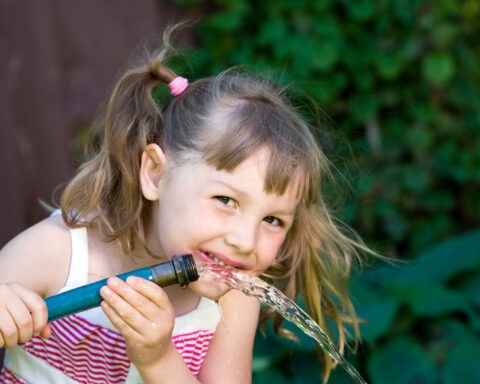 Child happily drinking water from a garden hose