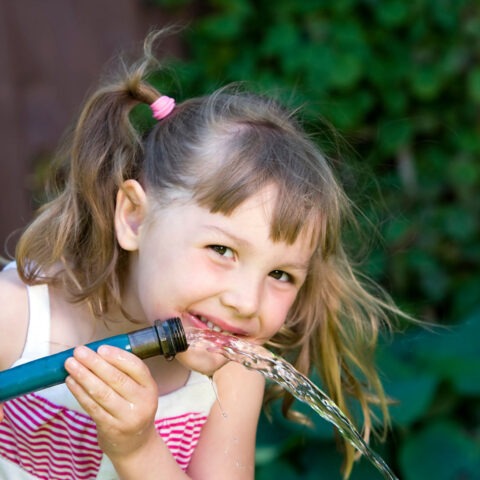 Child happily drinking water from a garden hose