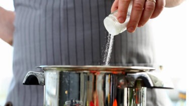 Close-up of person pouring salt into a pot on a stovetop.