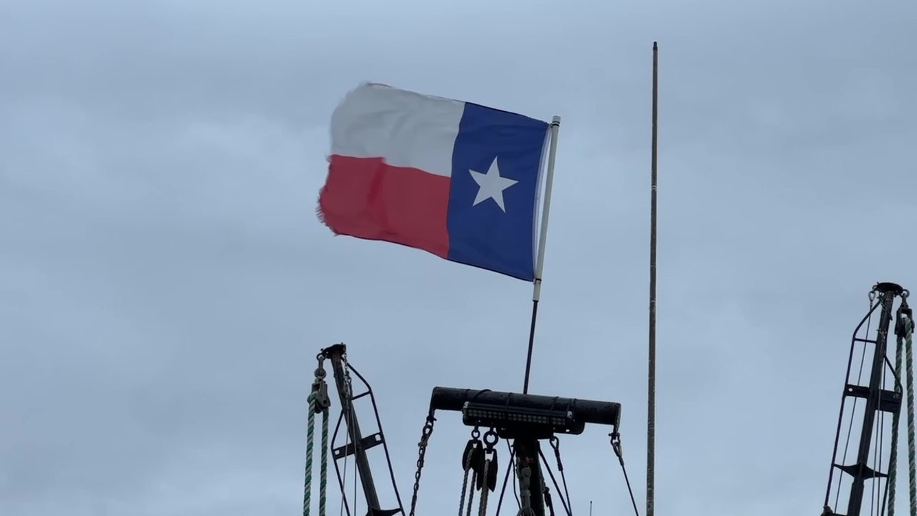 Texas state flag waving on a boat against cloudy sky.