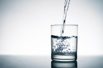 Close up of pouring fresh water into the clear glass from the bo