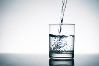 Close up of pouring fresh water into the clear glass from the bo