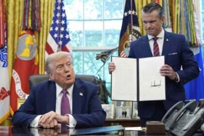 Donald Trump sits in the Oval Office as an aide displays a signed executive order