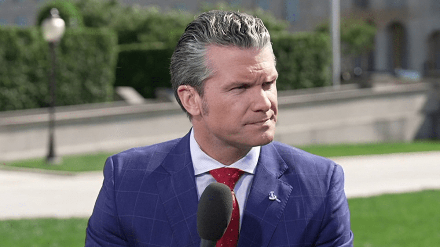 Pete Hegseth speaking outdoors with microphone in hand