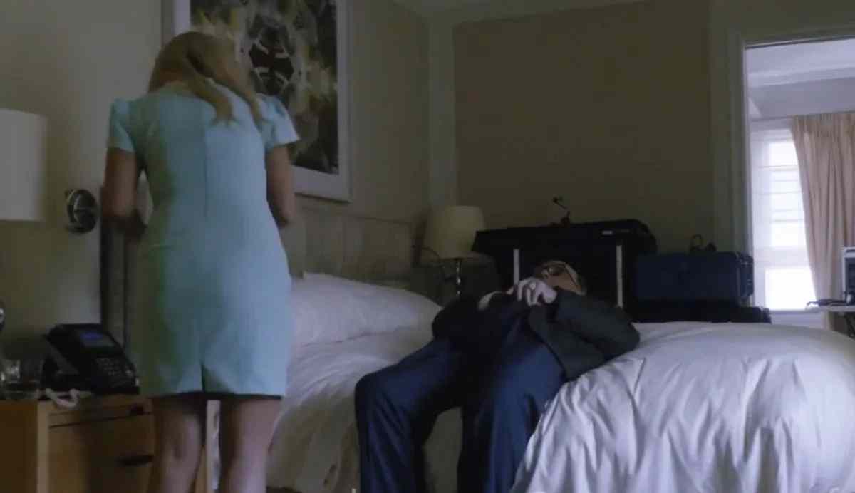 Rudy Giuliani reclines on a hotel bed with a woman standing nearby.