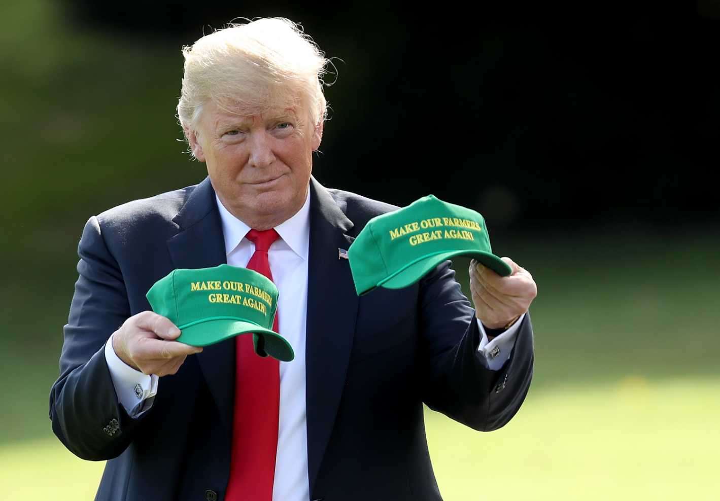 Donald Trump holding green “Make Our Farmers Great Again” hats during trade photo op.
