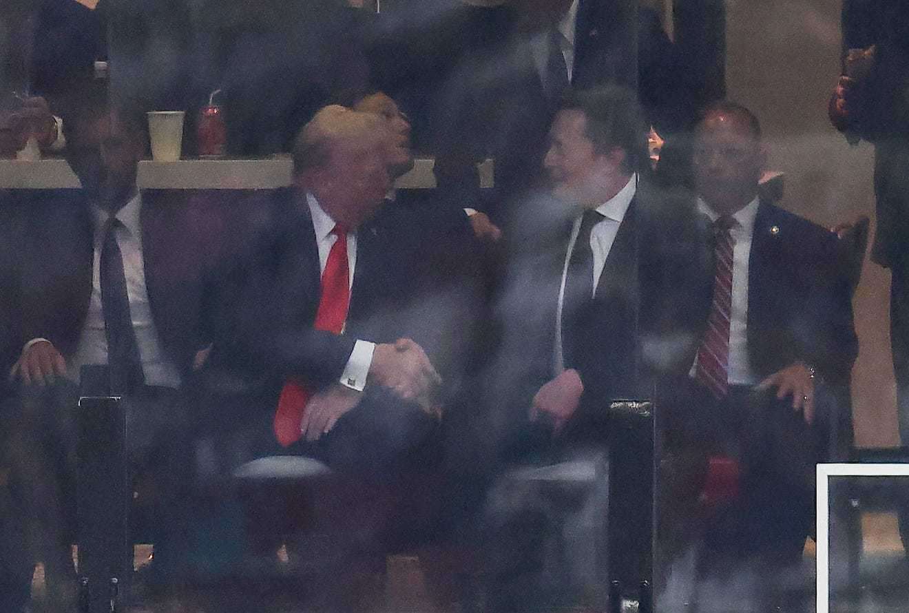 Donald Trump and Elon Musk shake hands while seated at an event.