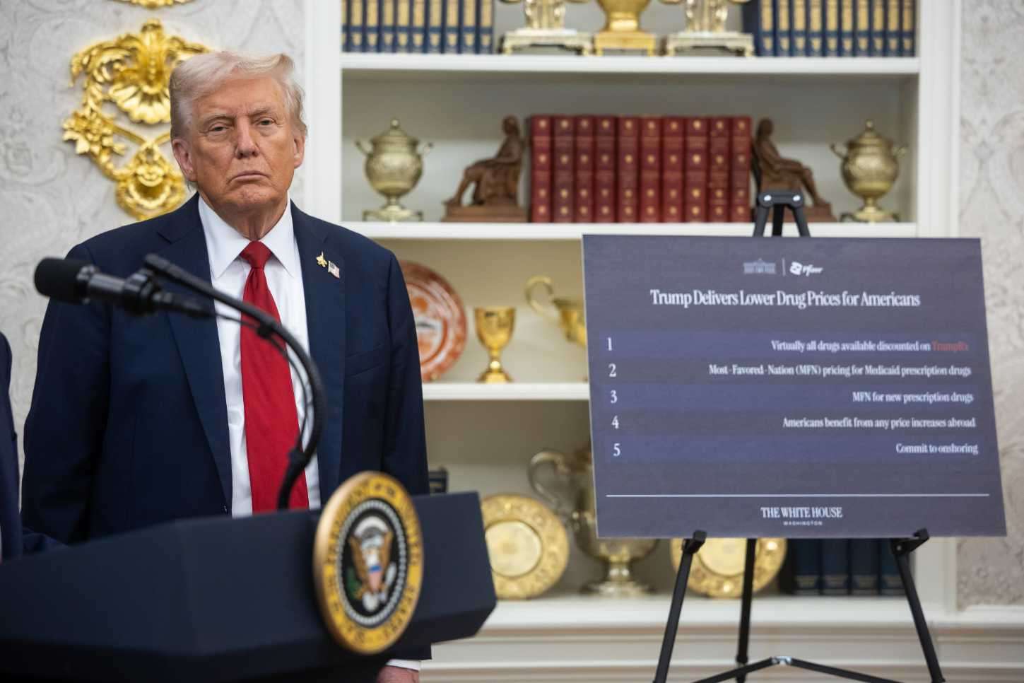 President Donald Trump stands next to a signboard announcing lower drug prices in the White House.