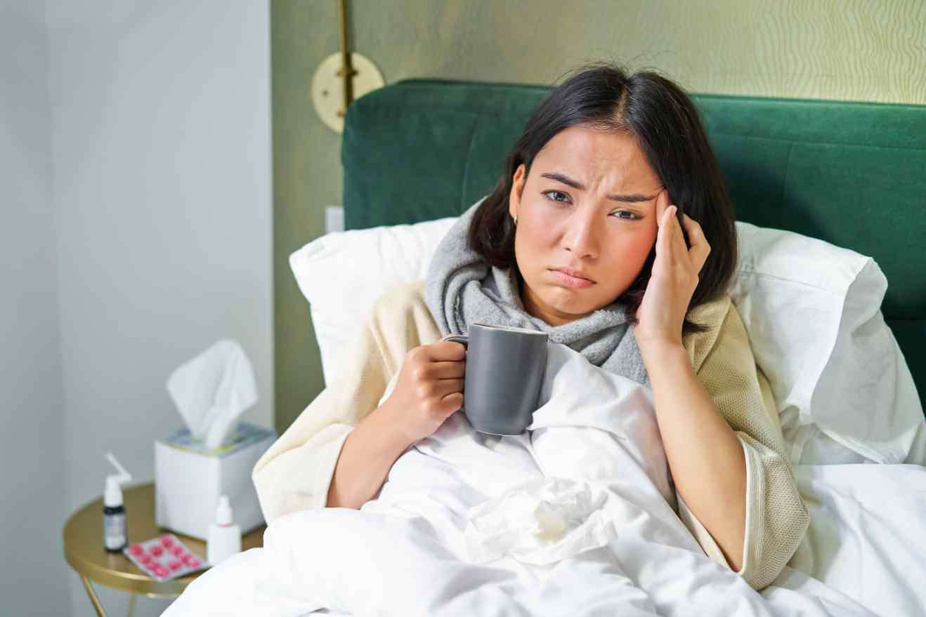 Woman sick in bed with cold holding a mug.