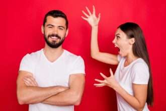 Man smiling confidently while woman yells at him against a red background.