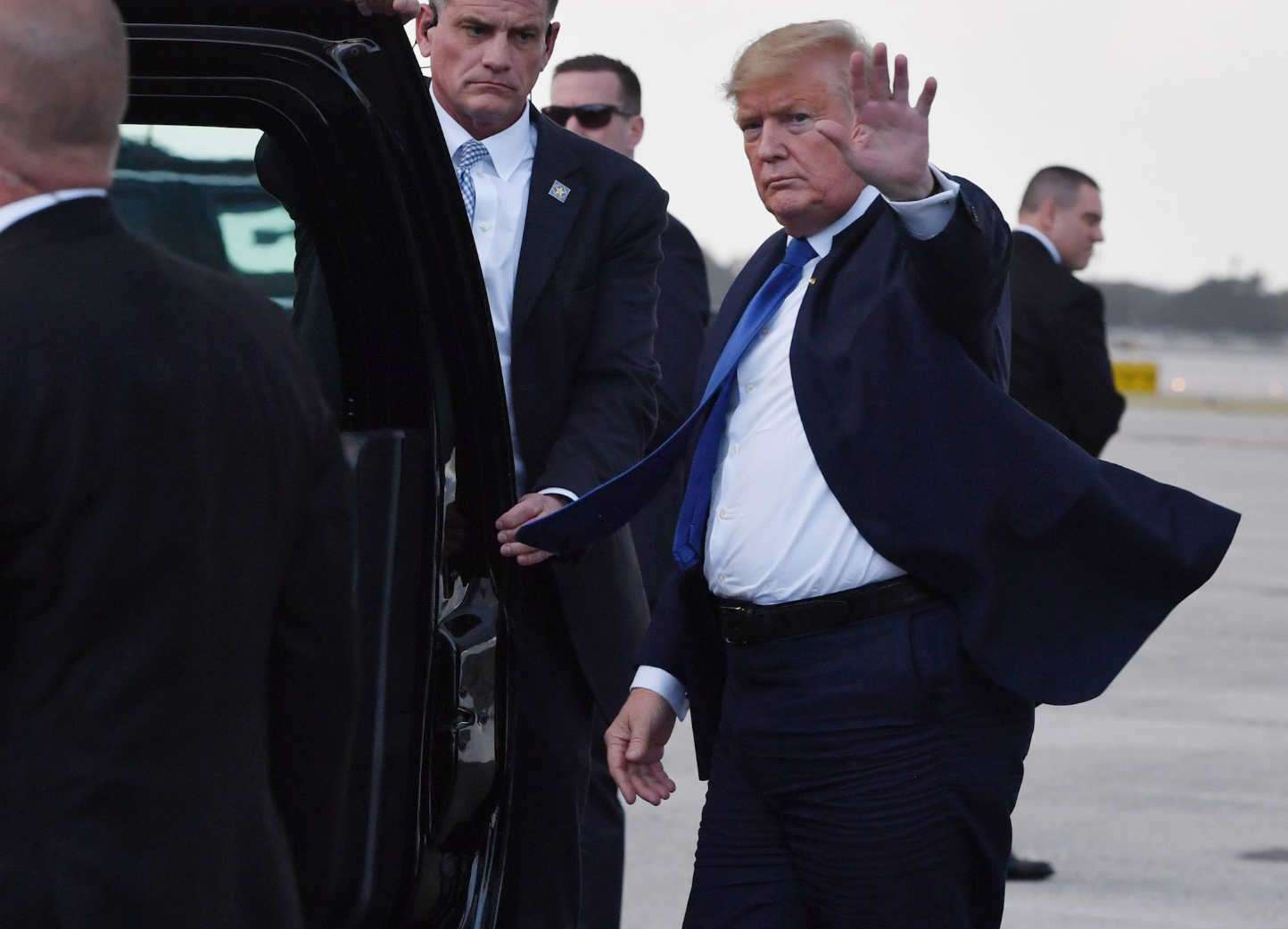 President Donald J. Trump waves while walking beside Secret Service agents.