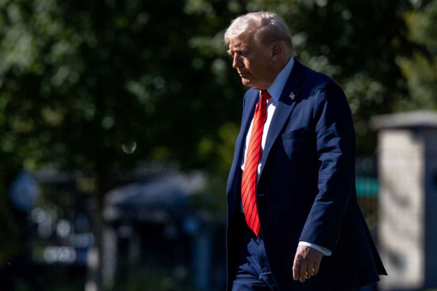 Donald Trump walking outside in a navy suit and red tie