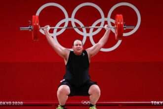 Olympic weightlifter performs a lift during competition with Olympic rings in background