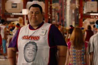 A Costco employee wearing a store vest standing in a busy warehouse-style retail environment.