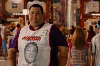 A Costco employee wearing a store vest standing in a busy warehouse-style retail environment.