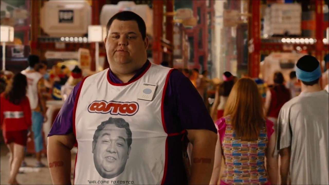 A Costco employee wearing a store vest standing in a busy warehouse-style retail environment.